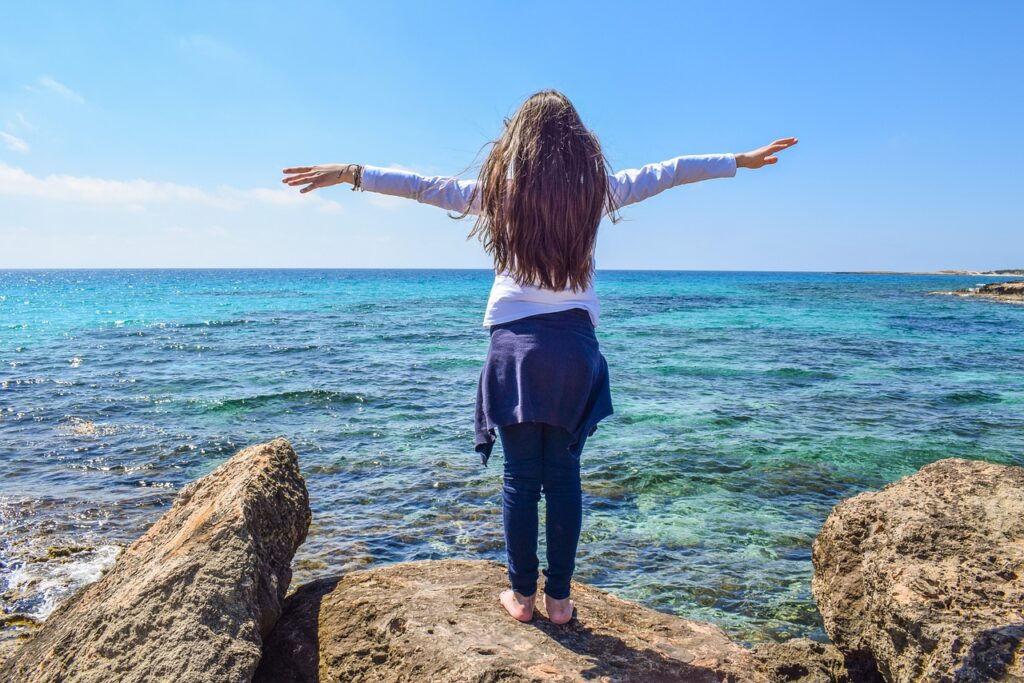 Femme profitant de l’air frais face à la mer, représentant une connexion profonde avec la nature.