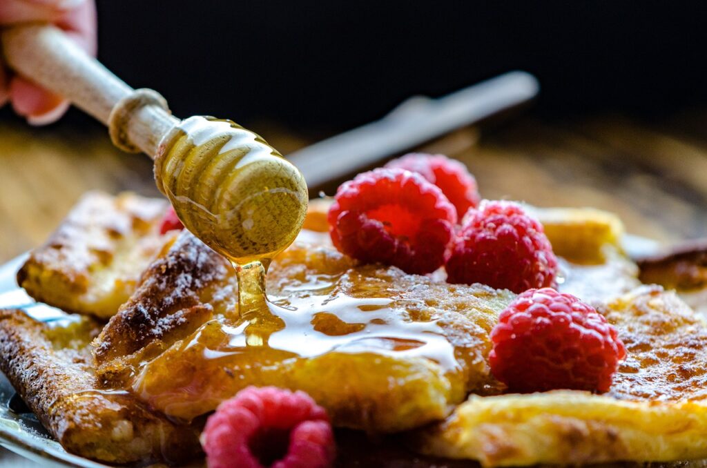 Pancakes accompagnés de framboises et nappés de miel artisanal, illustrant des idées gourmandes avec du miel.